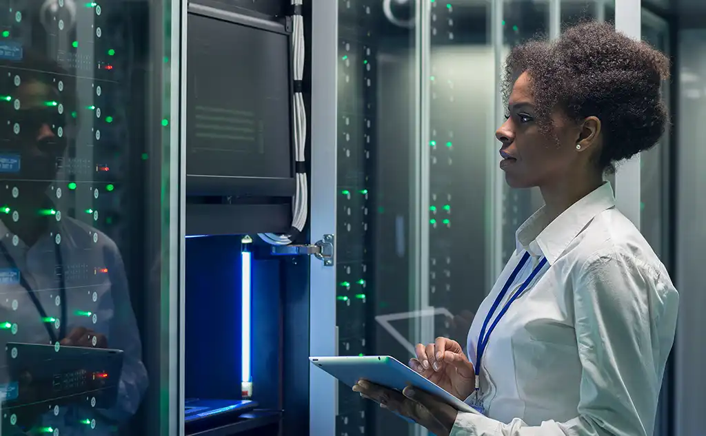 Medium shot of female technician working on a tablet in a data center full of rack servers running diagnostics and maintenance on the system.